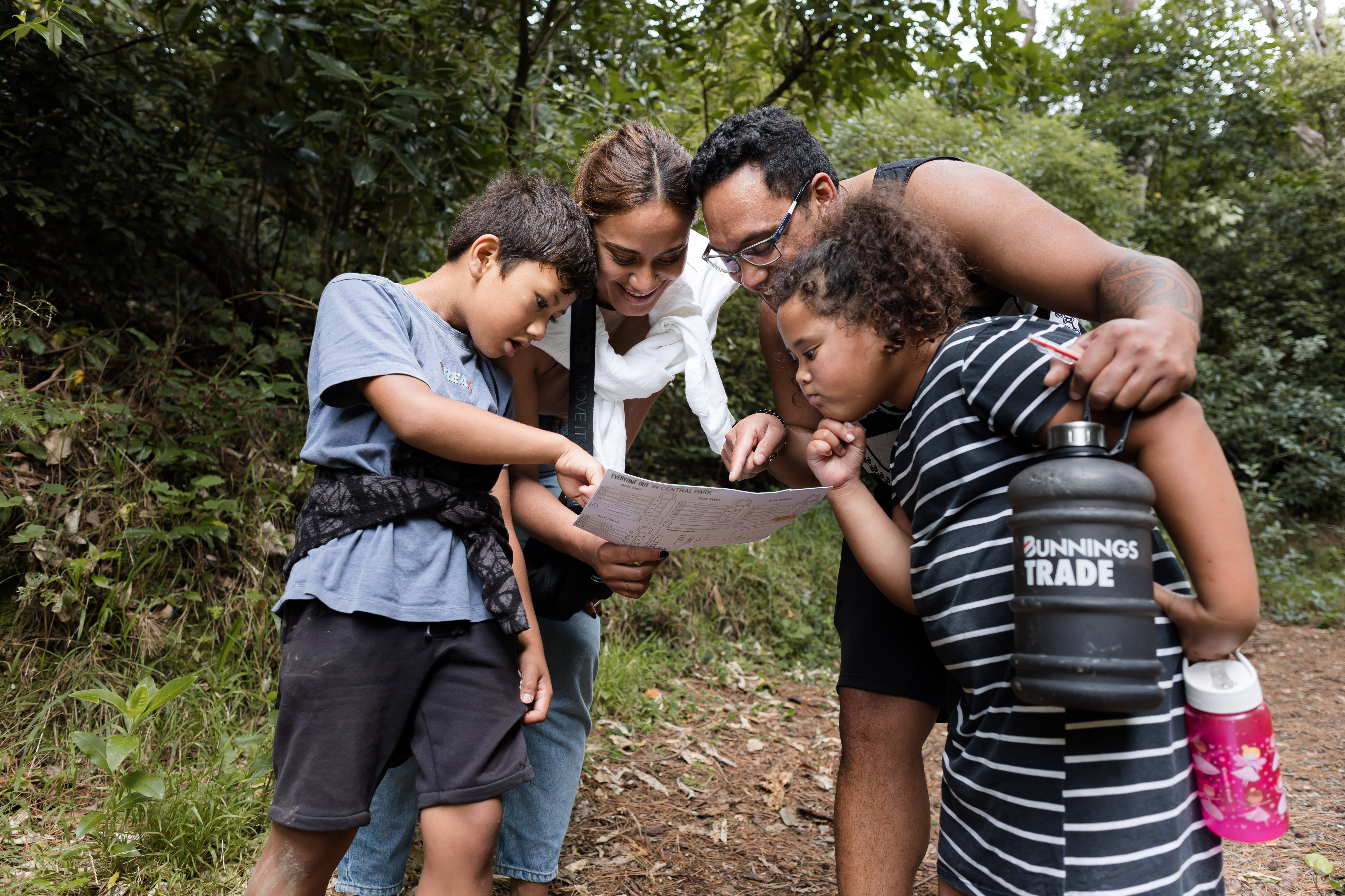 Two children and two adults stand in a sunny forest and consult a map