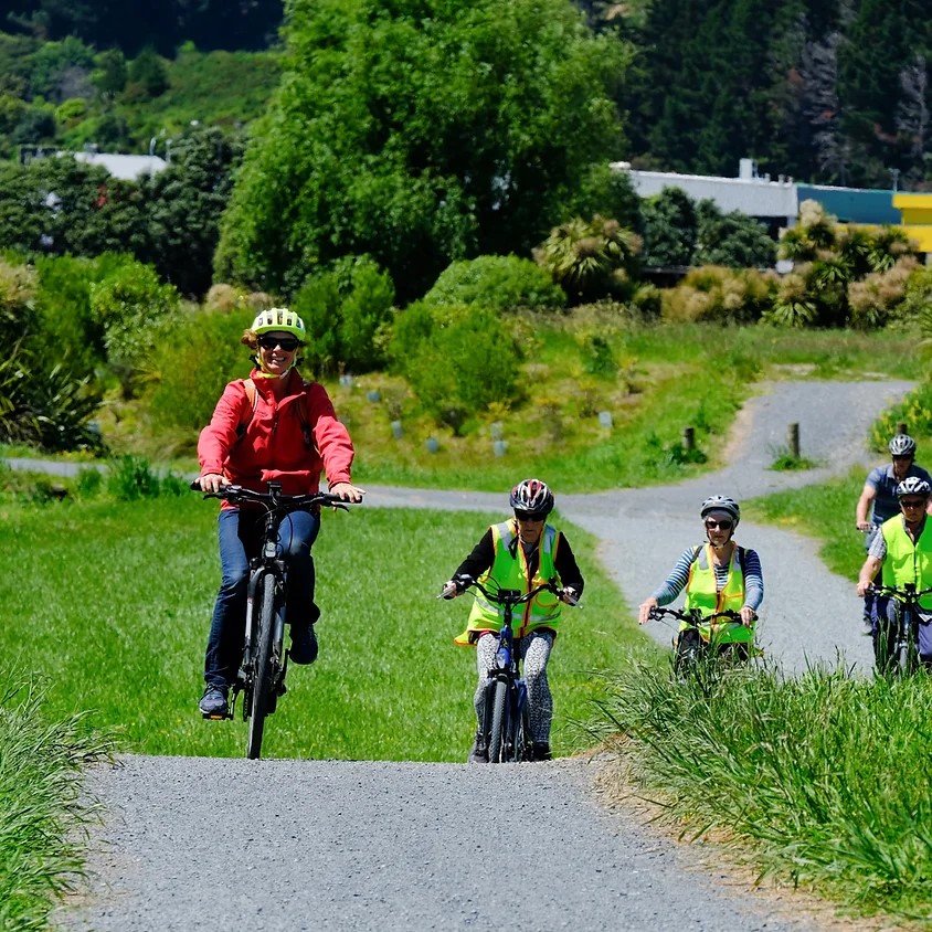 Five people on bikes cycle down a gravel track in a park on a sunny day