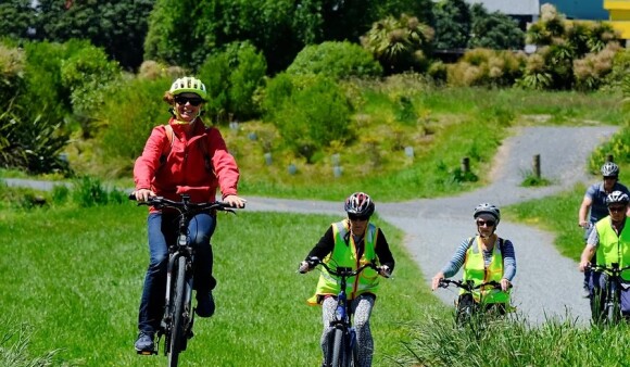 A row of cyclists bike through a green park on a sunny day